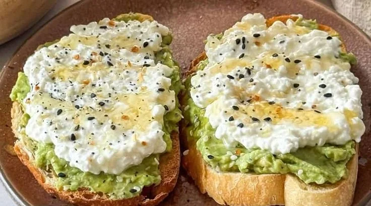Cottage cheese avocado toast topped with herbs and spices on a wooden table.
